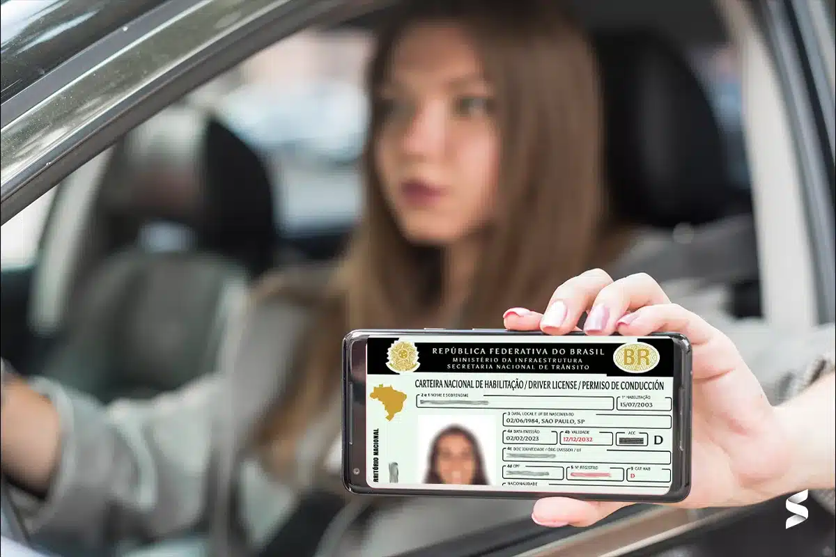 CNH renovada automaticamente Mulher segurando a versão digital da CNH no celular enquanto está dentro do carro, representando a renovação automática.