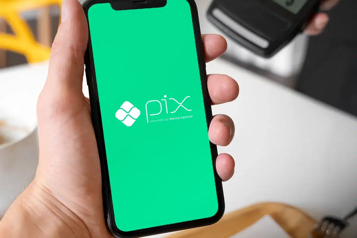 Tela do aplicativo Pix exibida em smartphone para pagamento rápido Mão segurando celular com tela do Pix ao lado de máquina de cartão
