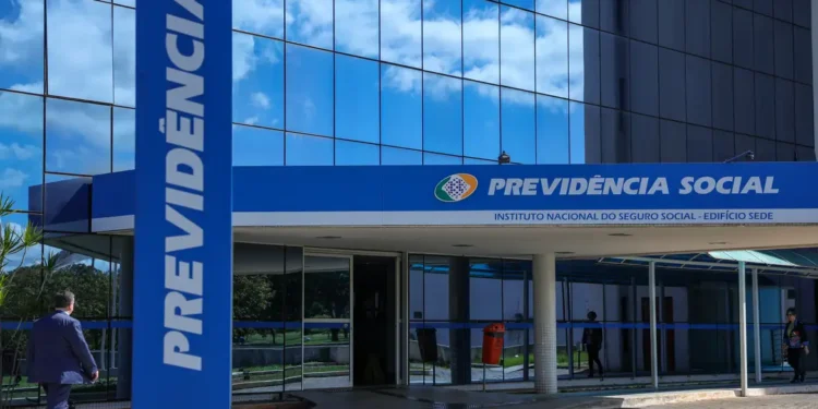Entrada principal da Previdência Social com vidro refletindo céu azul e pessoa caminhando