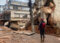 Imagem de um prédio desmoronado devido às chuvas em Minas Gerais, com um socorrista observando a cena de destruição, incluindo fios caídos e detritos espalhados pela rua.