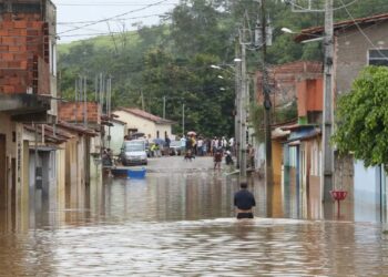 Rua alagada em cidade de Minas Gerais após fortes chuvas, cenário que motivou o anúncio de auxílio emergencial e antecipação de benefícios sociais.