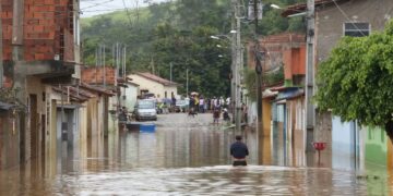 Rua alagada em cidade de Minas Gerais após fortes chuvas, cenário que motivou o anúncio de auxílio emergencial e antecipação de benefícios sociais.