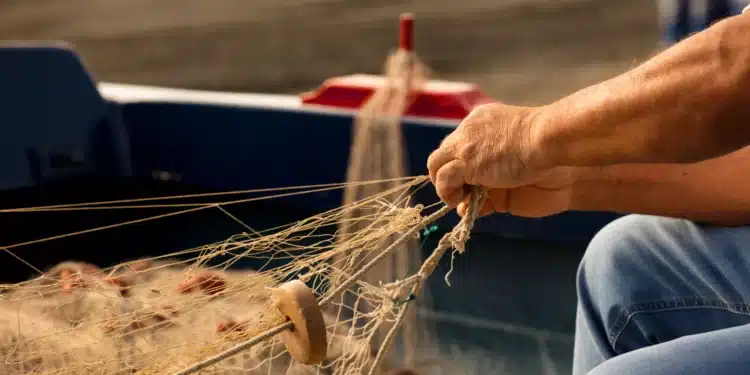 Pescador manuseando redes de pesca dentro de um barco, representando os trabalhadores que podem se beneficiar do Seguro-Defeso, cujo prazo foi ampliado até junho de 2026.