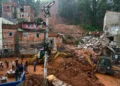 Trabalhadores e máquinas removem lama e destroços com casas destruídas por deslizamento sob chuva intensa