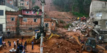 Trabalhadores e máquinas removem lama e destroços com casas destruídas por deslizamento sob chuva intensa