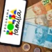 Smartphone exibindo logo do Bolsa Família junto a notas de R$ 20, 50 e 100 sobre mesa