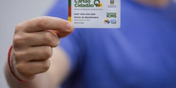 Pessoa segurando um Cartão Cidadão próximo à câmera, em fundo azul desfocado