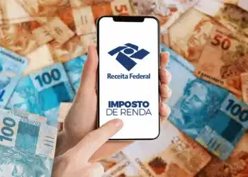 Mão apontando para celular com logo da Receita Federal cercado de cédulas de reais