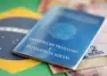 Carteira de Trabalho e Previdência Social azul posicionada sobre bandeira do Brasil com notas de 2 reais visíveis.