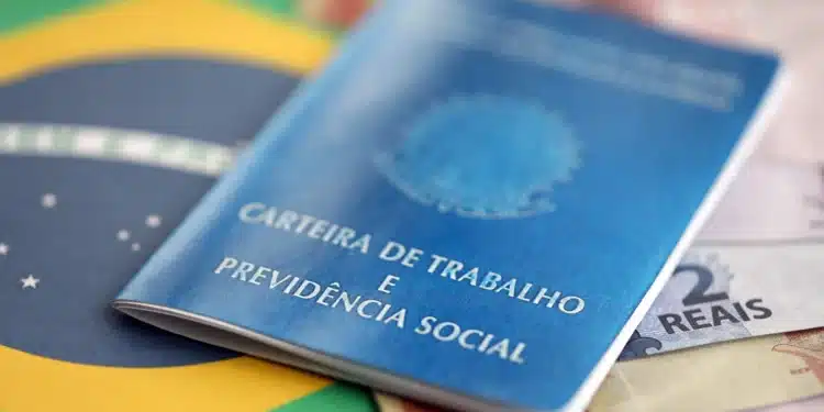 Carteira de Trabalho e Previdência Social azul posicionada sobre bandeira do Brasil com notas de 2 reais visíveis.