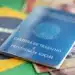 Carteira de Trabalho e Previdência Social azul posicionada sobre bandeira do Brasil com notas de 2 reais visíveis.