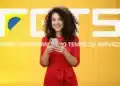 Mulher sorridente vestindo vestido vermelho segurando um celular com o logo do FGTS ao fundo amarelo