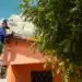 Técnico em escada instala antena parabólica digital Brasil Antenado em telhado de casa laranja.
