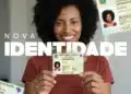 Uma mulher negra sorridente, com cabelos cacheados, segurando com as duas mãos o novo cartão da Carteira de Identidade Nacional (CIN). Ao fundo, há elementos gráficos do documento e o texto "NOVA IDENTIDADE" em destaque.