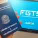 Mão segurando Carteira de Trabalho azul diante de monitor exibindo logo do FGTS e Caixa Econômica Federal