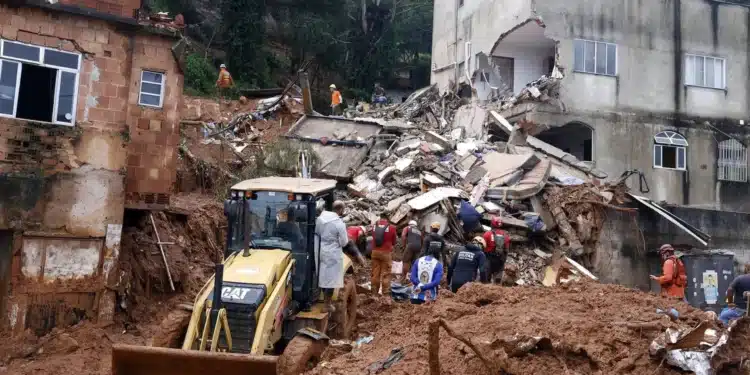 Equipes de bombeiros e maquinário escavam escombros de casas destruídas por deslizamento de terra em Minas Gerais.