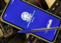 Um smartphone sobre um teclado de computador exibindo a tela azul do aplicativo Carteira de Trabalho Digital do Governo Federal do Brasil. Uma caneta esferográfica azul está pousada sobre o aparelho.
