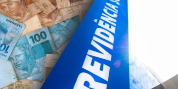 Cédulas de R$ 50 e R$ 100 ao lado de placa azul da Previdência Social com edifício espelhado ao fundo.