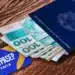 Carteira de trabalho azul com brasão, notas de R$ 100 e cartão PIS/Pasep Caixa sobre superfície de madeira.
