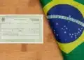Título de eleitor brasileiro com identificação biométrica ao lado da bandeira do Brasil sobre superfície de madeira.