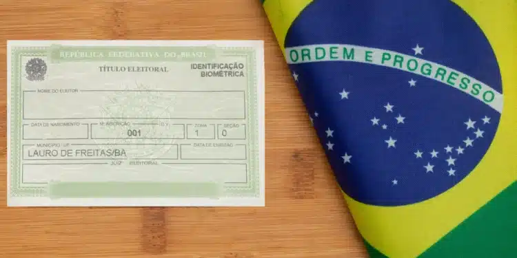 Título de eleitor brasileiro com identificação biométrica ao lado da bandeira do Brasil sobre superfície de madeira.