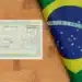 Título de eleitor brasileiro com identificação biométrica ao lado da bandeira do Brasil sobre superfície de madeira.