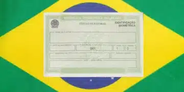 Título de eleitor com identificação biométrica posicionado sobre a bandeira do Brasil verde e amarela.