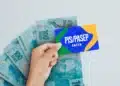 Mão segura cartão azul, verde e amarelo com texto PIS/PASEP e logo Caixa sobre notas de R$100
