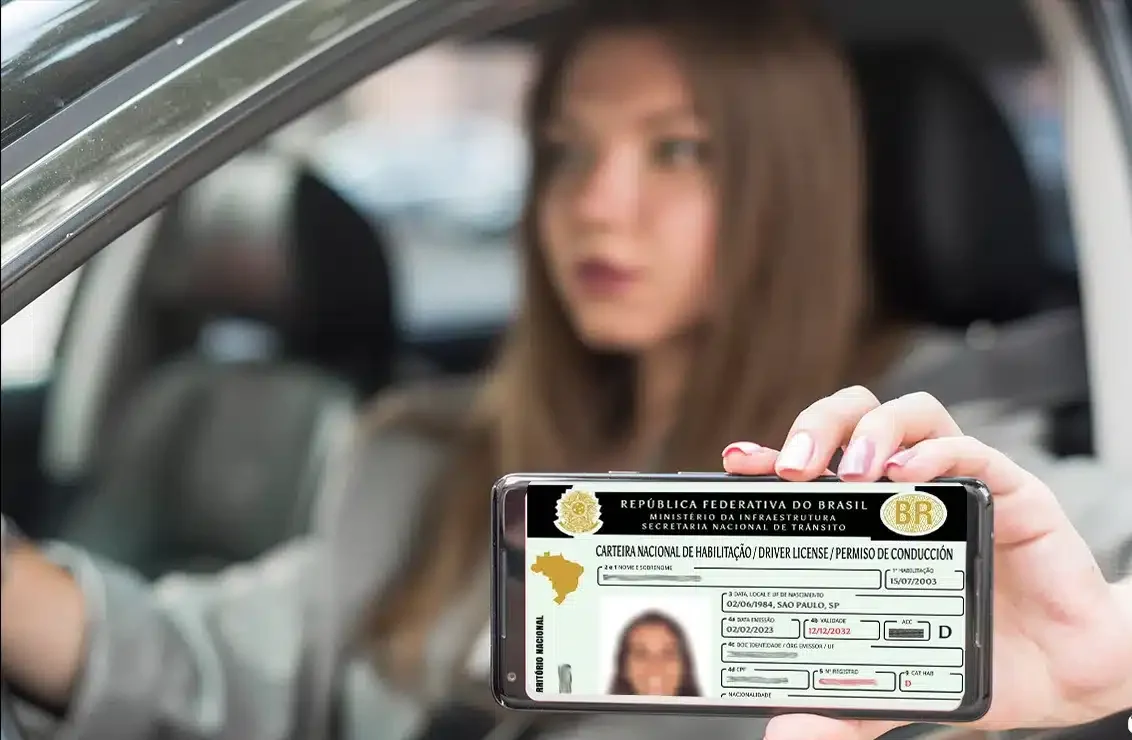 Mulher ao volante observa enquanto mão segura celular exibindo CNH digital brasileira com dados visíveis