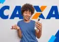 Jovem negra com cabelo crespo, camiseta azul, segura iPhone branco, olhando a tela com expressão de surpresa e gesticulando