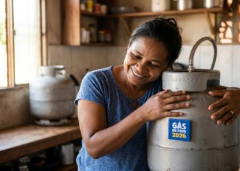 Mulher sorridente de camiseta azul abraça botijão de gás Ultragaz com adesivo Gás do Povo 2026 em cozinha humilde