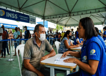 Homem de máscara conversa com servidora do INSS em tenda do programa Governo na Rua em Salvador