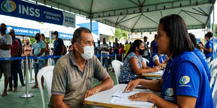 Homem de máscara conversa com servidora do INSS em tenda do programa Governo na Rua em Salvador
