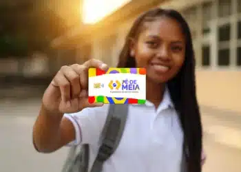 Jovem estudante negra com uniforme branco e mochila mostrando cartão do Pé-de-Meia
