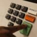 Mão pressionando tecla verde Confirma em urna eletrônica com teclado numérico, botões Branco e Corrige