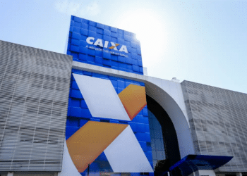Fachada azul de agência Caixa Econômica Federal com logo X estilizado em branco e laranja contra céu azul.