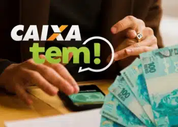 Mãos manuseiam celular com aplicativo Caixa Tem ao lado de notas de R$ 100