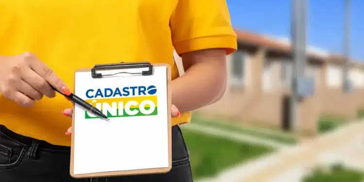 Pessoa segurando prancheta com logotipo do Cadastro Único em frente a conjunto habitacional