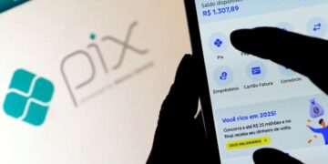 Pessoa utilizando aplicativo bancário no celular para realizar um PIX, com o logotipo do PIX em destaque ao fundo em uma tela de computador.