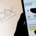 Pessoa utilizando aplicativo bancário no celular para realizar um PIX, com o logotipo do PIX em destaque ao fundo em uma tela de computador.