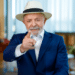 Presidente Lula vestindo paletó azul e chapéu panamá claro, apontando o dedo indicador para a frente em um gesto de ênfase, em um ambiente interno iluminado.