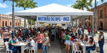 Centenas de pessoas em fila sob tenda branca com faixa "Mutirão do BPC - INSS" em praça de Caruaru com palmeiras e prédios históricos