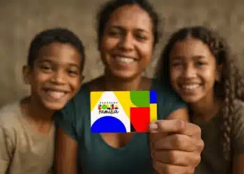 Mãe e dois filhos sorriem mostrando cartão colorido do Programa Bolsa Família com fundo desfocado