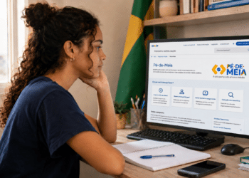 Jovem mulher observa tela de computador com programa Pé-de-Meia do MEC ao lado de caderno e livros