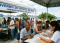 Atendentes recebem cidadãos em mesas sob tenda branca com faixa "Governo do Brasil na Rua" à beira-mar em Floripa