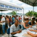 Atendentes recebem cidadãos em mesas sob tenda branca com faixa "Governo do Brasil na Rua" à beira-mar em Floripa