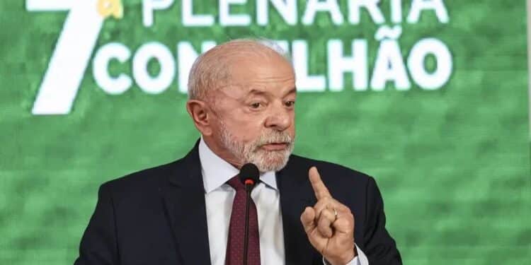 Lula em paletó escuro e gravata, fala ao microfone, dedo em riste, painel verde com “7ª Plenária Conselhão” ao fundo