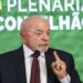 Lula em paletó escuro e gravata, fala ao microfone, dedo em riste, painel verde com “7ª Plenária Conselhão” ao fundo