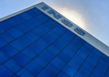 Prédio do INSS com fachada de vidro azul refletindo o céu, letras grandes no topo