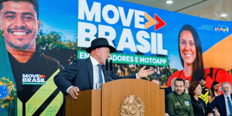 Presidente discursando com chapéu em evento Move Brasil, painel destaca entregador e entregadora sorrindo ao fundo